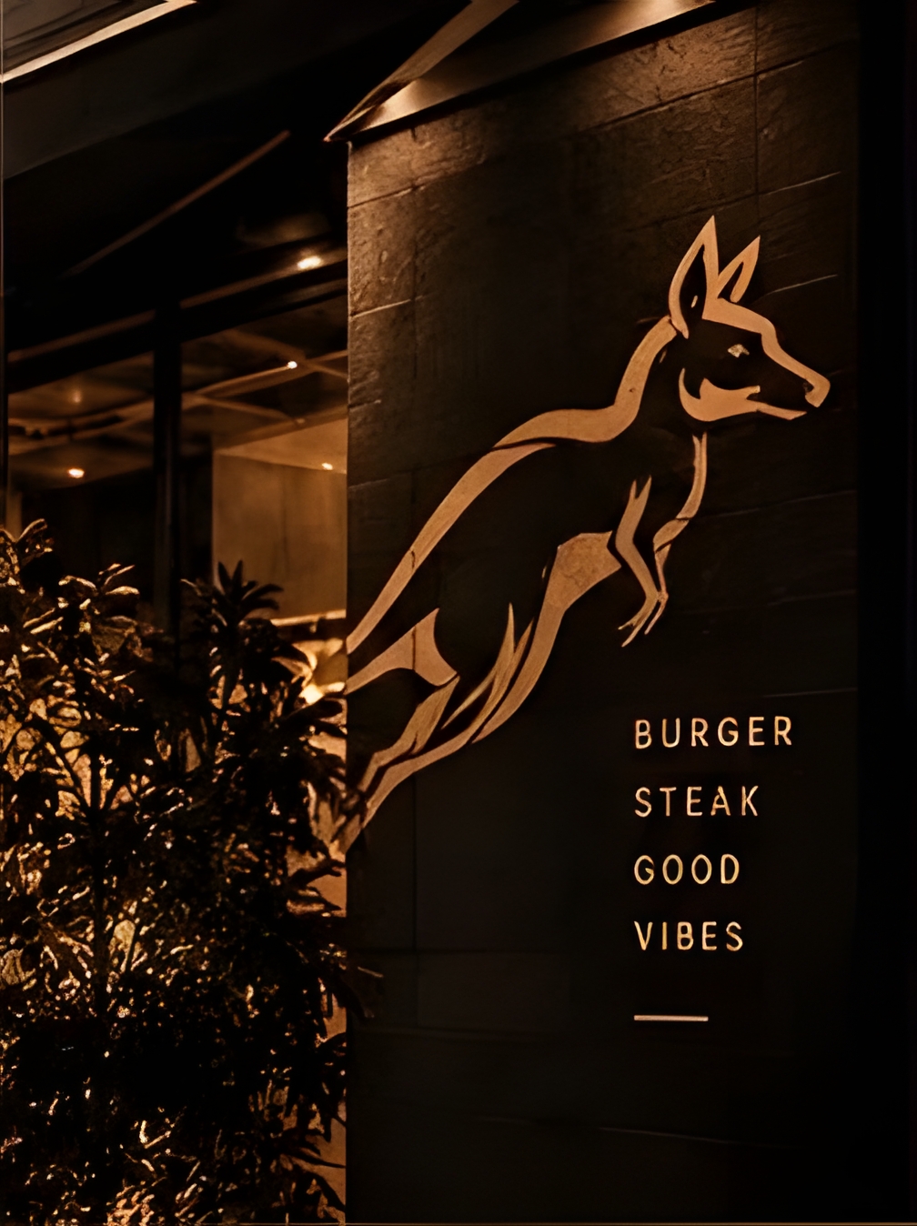 Fachada do Canguru Burger Steakhouse com letreiro iluminado em dourado — canguru saltando e texto Burger Steak Good Vibes