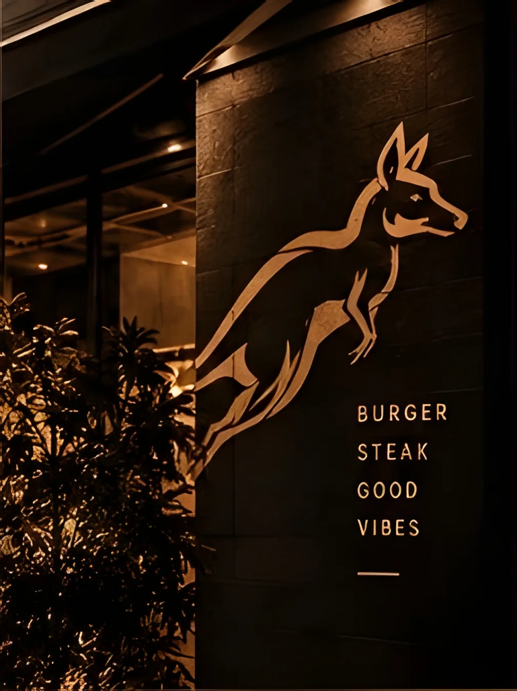 Fachada do Canguru Burger Steakhouse com letreiro iluminado em dourado — canguru saltando e texto Burger Steak Good Vibes